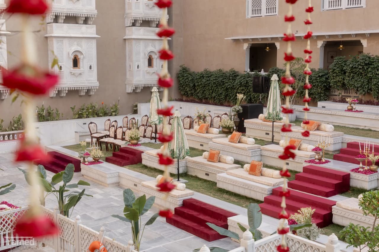 Ivory courtyard with red floral garlands and tiered seating — Devanshi & Rohan, Taj Lalit Bagh, Udaipur